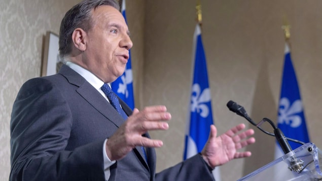 Le premier ministre François Legault devant un micro, avec en arrière-plan deux drapeaux du Québec.