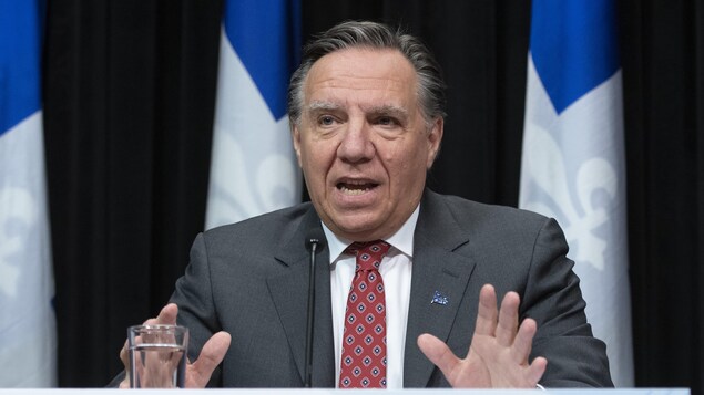 Le premier ministre parle devant des drapeaux du Québec.