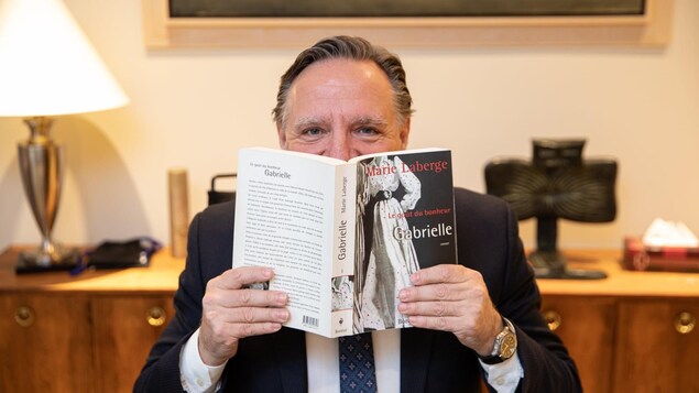 L'homme tient le premier tome de la trilogie, « Gabrielle », dans ses mains, devant son visage.