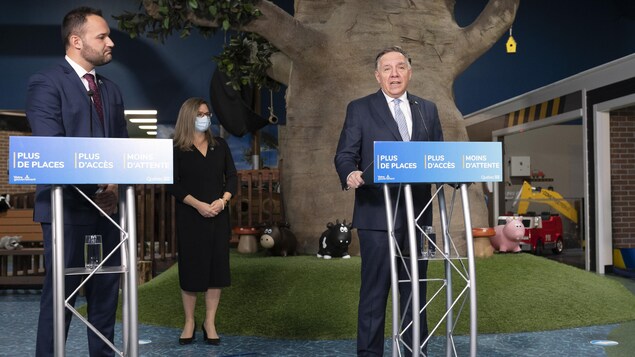 François Legault parle debout devant un arbre géant et Mathieu Lacombe à sa droite le regarde. 