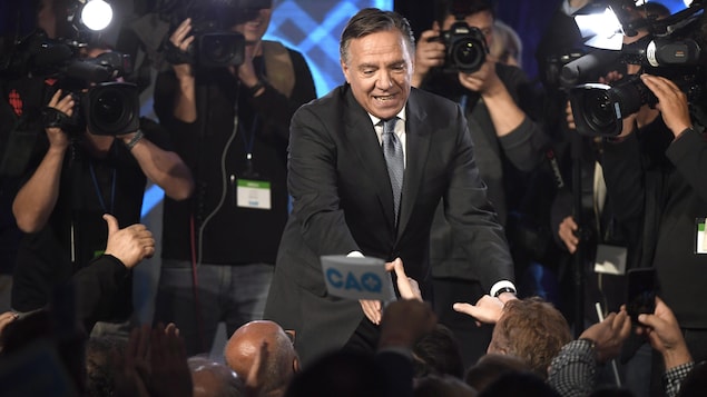 Le chef de la Coalition avenir Québec, François Legault, distribue les poignées de main à des militants de sa formation politique devant les caméras.