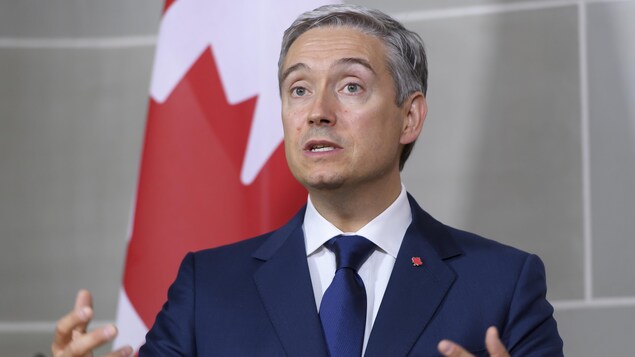 Il parle devant un drapeau du Canada.