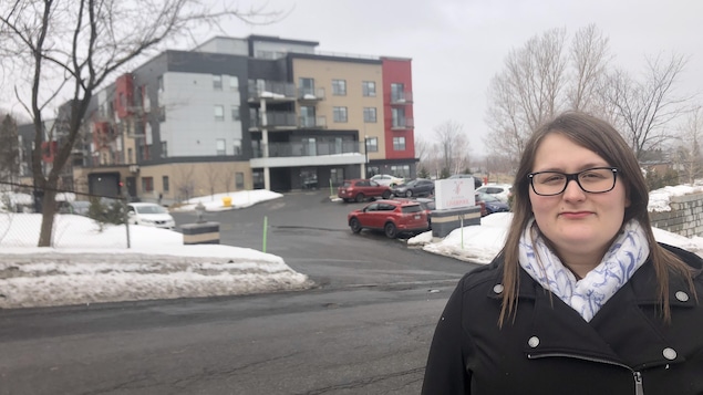 Une femme debout devant un immeuble à logements.