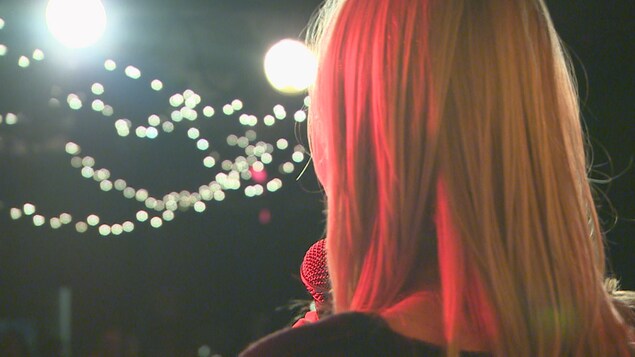 Une chanteuse qui tient un micro devant une foule dans la noirceur et des petites lumières.
