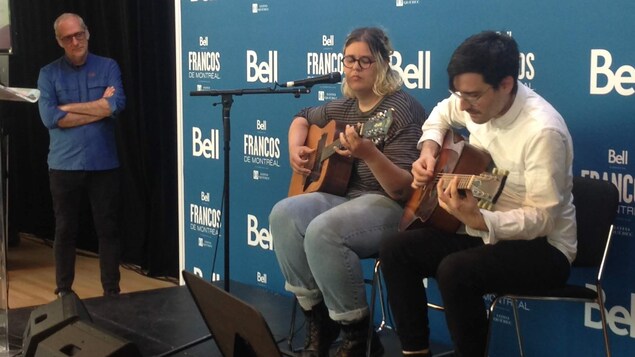 Le directeur de la programmation des Francos, Laurent Saulnier (à gauche), observe Safia Nolin et Joseph Marchand, qui sont assis sur des chaises sur une scène, lors de l'annonce des grands concerts de clôture du festival. Le directeur de la programmation des Francos, Laurent Saulnier (à gauche), observe Safia Nolin et Joseph Marchand, qui sont assis sur des chaises sur une scène, lors de l'annonce des grands concerts de clôture du festival.