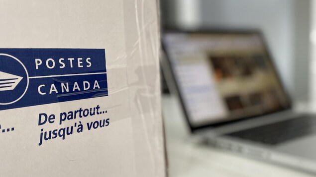 Une boîte de Postes Canada est posée sur une table à côté d'un ordinateur portable.