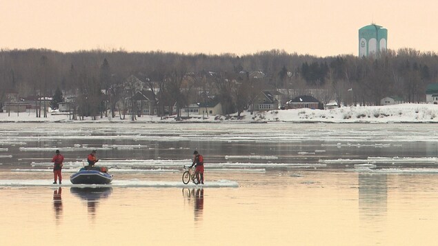 Trois hommes, un vélo et un bateau pneumatique sur une banquise sur le fleuve Saint-Laurent.