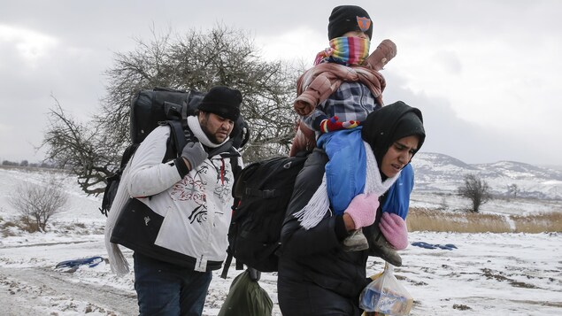 Un couple, dont la mère porte son enfant sur son dos, traverse un champ couvert de neige en Serbie Un couple, dont la mère porte son enfant sur son dos, traverse un champ couvert de neige en Serbie