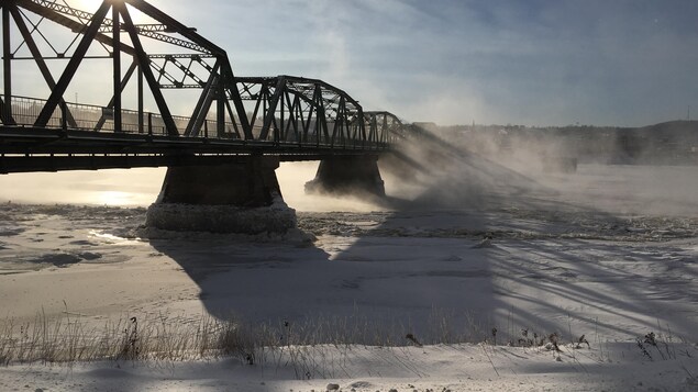 Un pont surplombe une rivière en hiver. 
