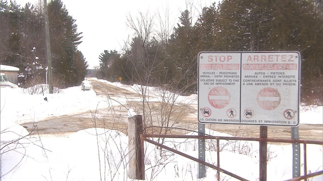 Une affiche interdit le passage de la frontière. En arrière-plan,un chemin enneigé dans la forêt. Une affiche interdit le passage de la frontière. En arrière-plan,un chemin enneigé dans la forêt.