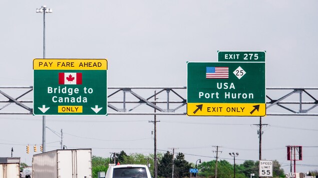 Deux affiches pour indiquer l'approche de la frontière canadienne au-dessus d'une route.