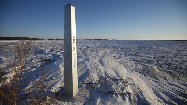Un marqueur à la frontière entre le Canada et les États-Unis au Manitoba, dans un champ couvert de neige.