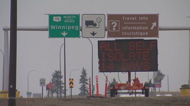 Un panneau lumineux et des affiches autour d'une route.