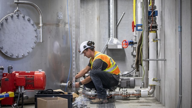 Un ouvrier dans une usine, accroupi près d'un réservoir en métal, en juin 2023, à Chilliwack, en Colombie-Britannique.