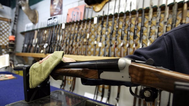 Un vendeur dans un magasin de chasse d'Ottawa essuie une arme d'épaule, devant un mur où sont présentées de nombreuses autres armes.
