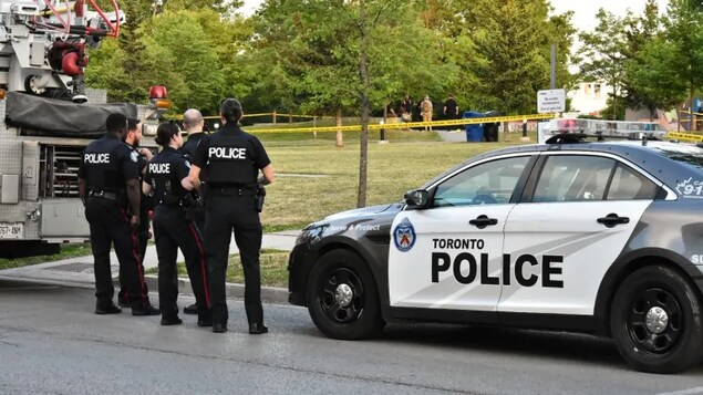 Des policiers debout près d'une autopatrouille et l'entrée d'un parc.
