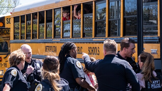 Des enfants regardent par les fenêtres dans un autobus. Des policiers sont debout, à l'extérieur du véhicule.