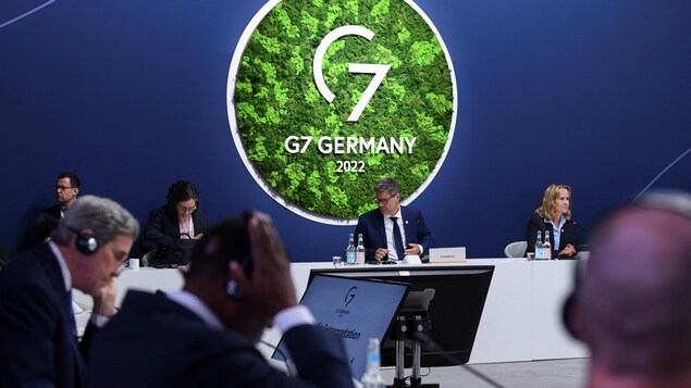 Des personnes assises à leur bureau devant le logo du G7. 