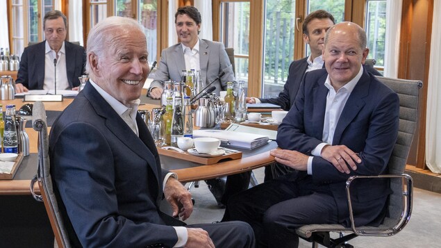 Des dirigeants du G7,  assis à une table ronde, sourient pour les photographes. 