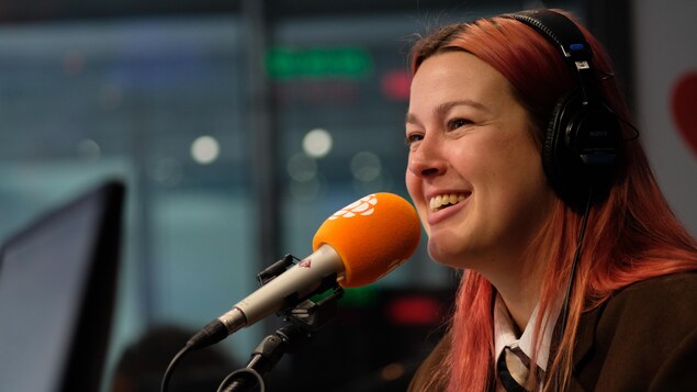 Une femme avec les cheveux longs derrière un micro dans un studio de radio.