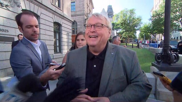 Gaétan Barrette, souriant, entouré de journalistes.