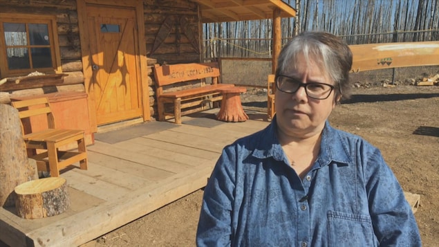 Gail Gallupe se tient devant une maison en bois. Gail Gallupe se tient devant une maison en bois.