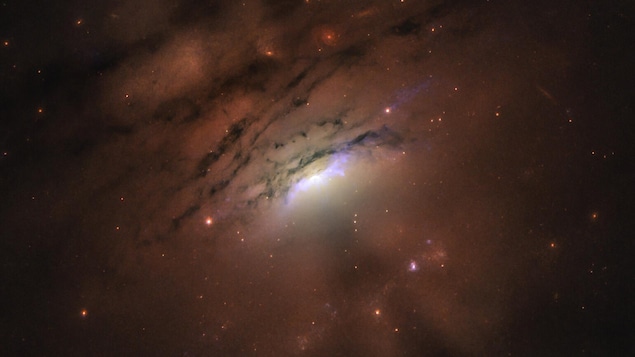 Cette image de la galaxie IC 5063 révélant un mélange de rayons lumineux et d'ombres sombres provenant de son noyau, siège d'un trou noir supermassif.