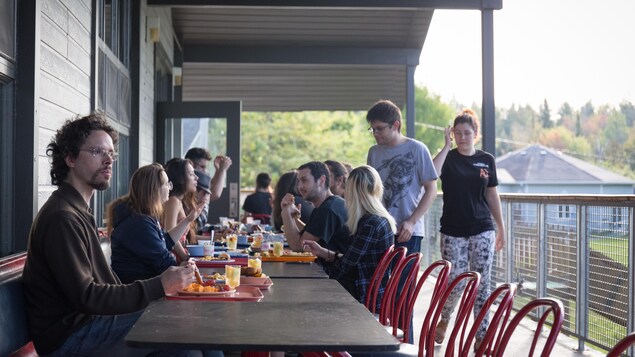 Un jeune homme assis à la table d'une cafétéria, sur la terrasse extérieure, et regarde le paysage au loin. Un jeune homme assis à la table d'une cafétéria, sur la terrasse extérieure, et regarde le paysage au loin.