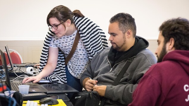 Une jeune femme debout utilise l'ordinateur portable de son coéquipier, qui la regarde travailler. Une jeune femme debout utilise l'ordinateur portable de son coéquipier, qui la regarde travailler.