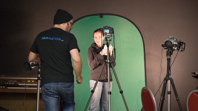 Une jeune femme pose devant un écran vert, pendant que son coéquipier la photographie. Une jeune femme pose devant un écran vert, pendant que son coéquipier la photographie.
