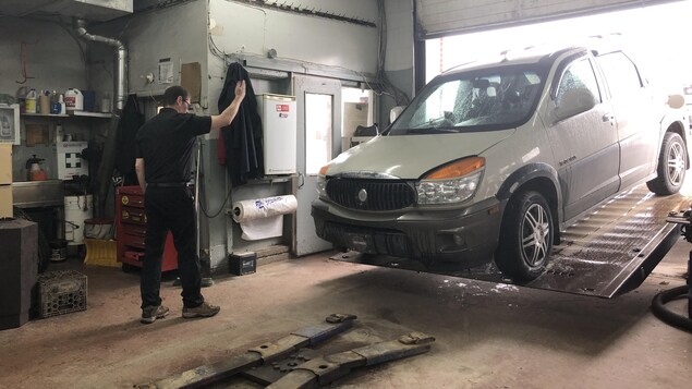 Un garagiste devant une voiture sur un élévateur dans un garage.