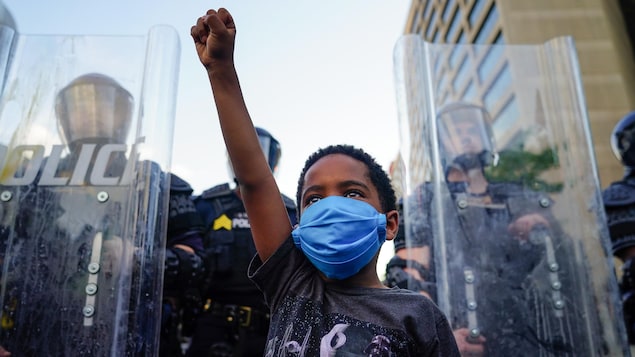 Un garçonnet noir lève le poing, devant des policiers protégés par des boucliers