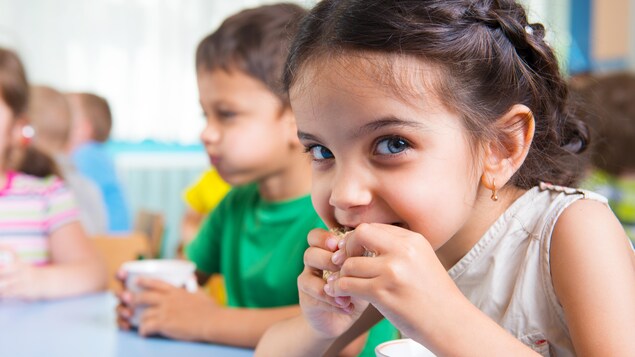 Des enfants assis à une table mangent une collation en buvant un verre de lait.