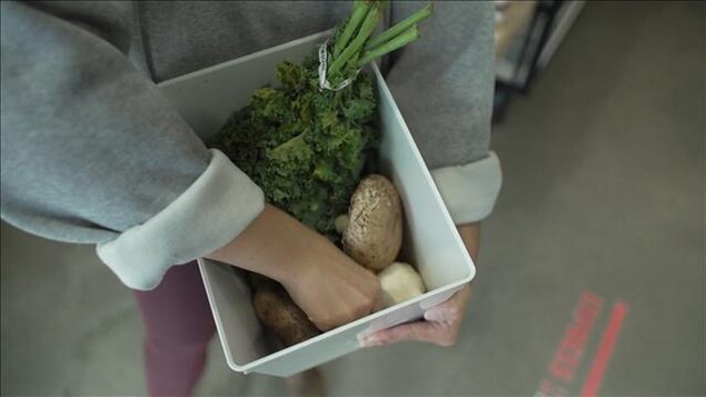 Une femme tient un contenant de légumes.
