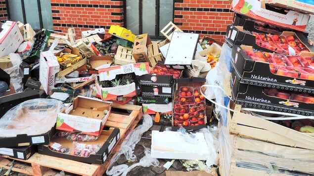 Des contenants de fruits sont empilés derrière un bâtiment.
