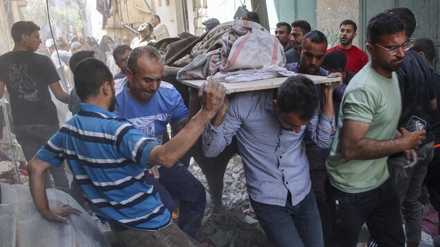 Un groupe d'hommes portant sur une planche un homme tué dans un bombardement à Gaza.