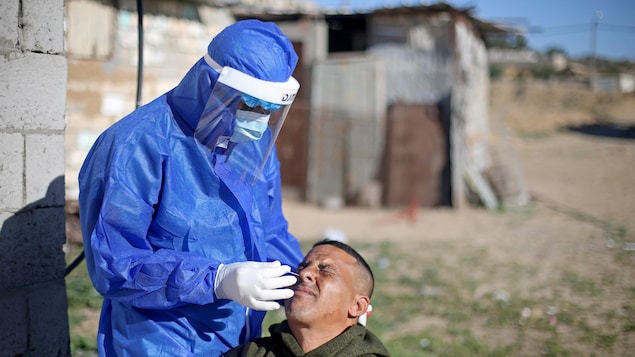 Un travailleur de la santé portant de l'équipement de protection met un écouvillon dans le nez d'un homme.