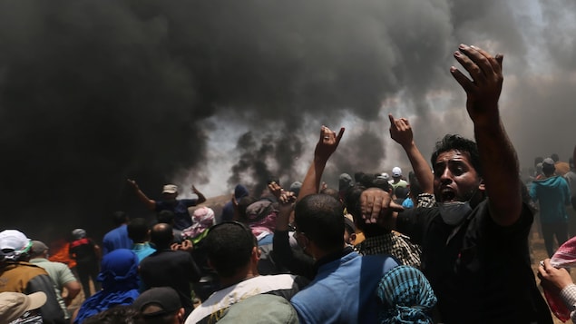 Des dizaines de Palestiniens manifestent dans la bande de Gaza, près d'un imposant nuage de fumée noire, attribuable à des pneus brûlés.