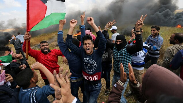 Des manifestants palestiniens lèvent les bras en l'air, alors que de la fumée les entoure.