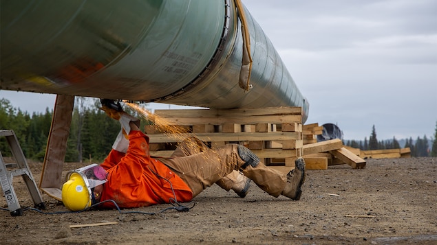 Un travailleur fait des travaux de soudure allongé sous un grand tuyau.