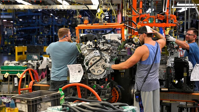 Trois hommes travaillent autour d'un moteur.