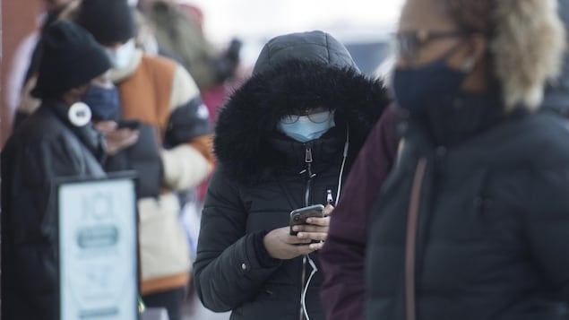 Des gens portant un masque font la file à l'extérieur d'un commerce.