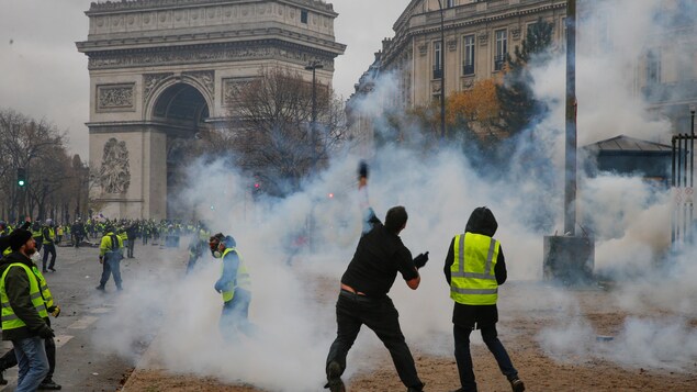 Des manifestants des « gilets jaunes », enfumés de gaz lacrymogènes, lancent des projectiles près de l'Arc de triomphe à Paris.