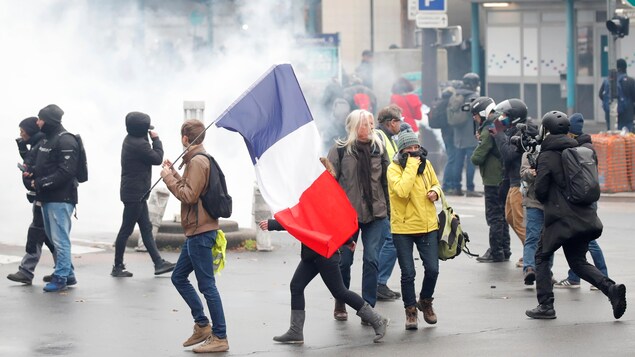 Des manifestants sur fond de gaz lacrymogène. L'un d'eux tient un drapeau de la France.
