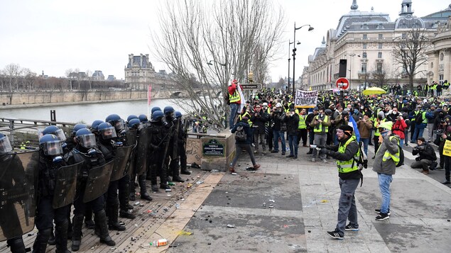 Des gilets jaunes en face de policiers antiémeute sur le bord de la Seine