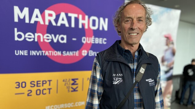 Il pose devant une affiche du marathon de Québec. 