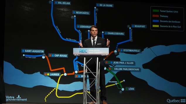 François Bonnardel derrière le podium lors de la conférence de presse avec la carte du Réseau express de la Capitale en arrière plan.