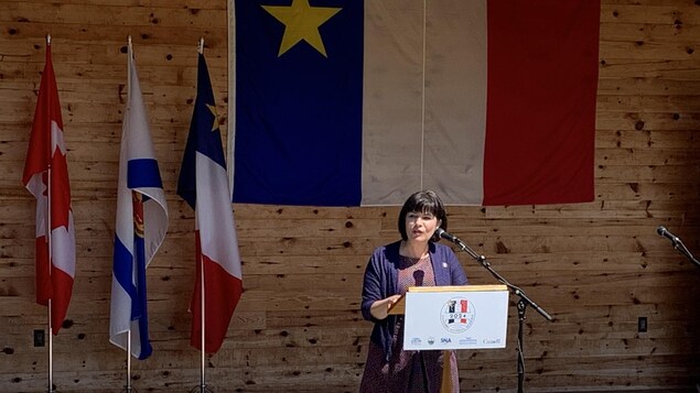 Ginette Petitpas Taylor, ministre des Langues officielles et ministre responsable de l’Agence de promotion économique du Canada atlantique, sur un estrade en train de faire une annonce. Derrière elle, des drapeaux de l'Acadie, de la Nouvelle-Écosse et du Canada. 