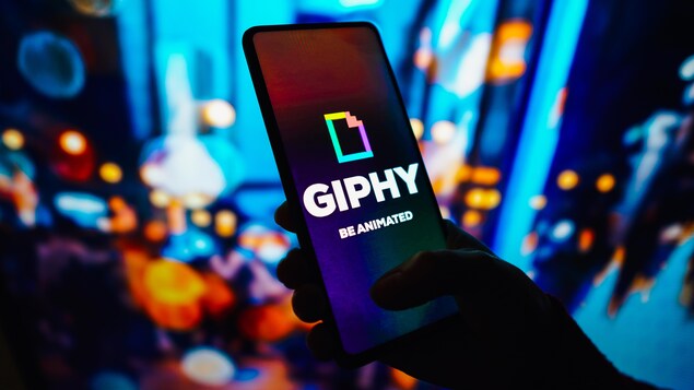 Une personne tient un téléphone intelligent montrant le logo de Giphy. 