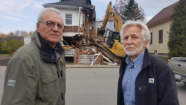 Deux hommes posent devant un bâtiment déconstruit.